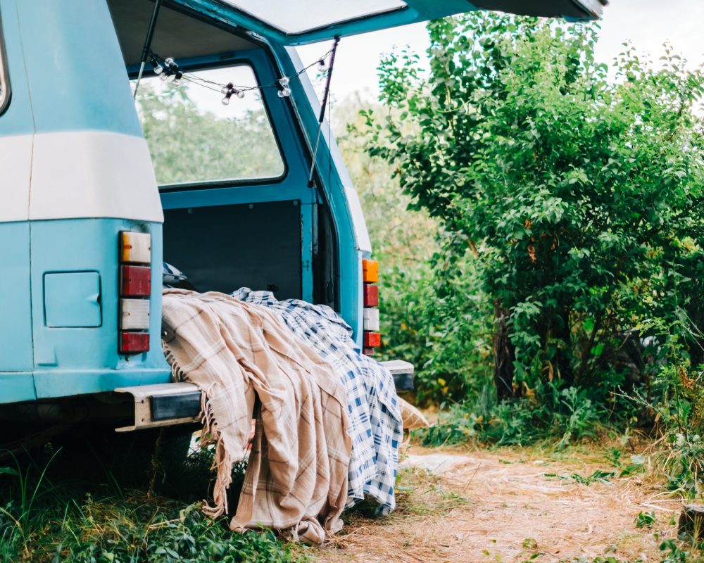 blue-white-retro-van-in-nature-with-cozy-decorations-blanket-and-pillow