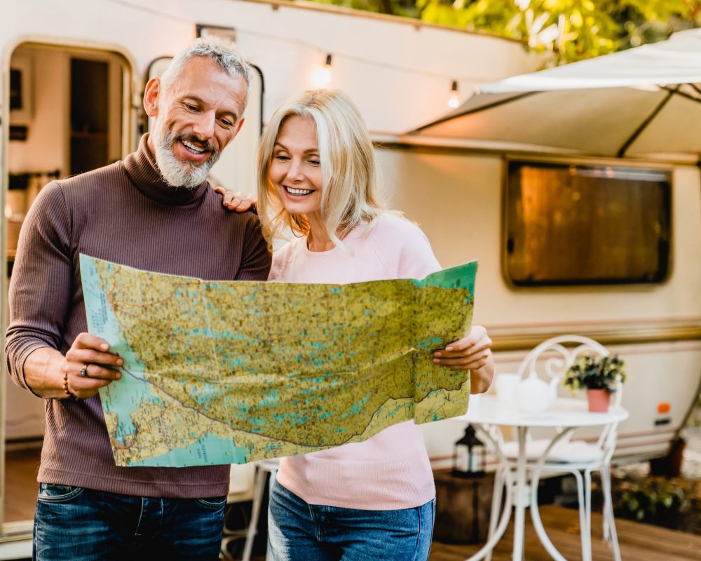 energetic-elderly-european-couple-looking-at-the-map-with-their-caravan-home-behind