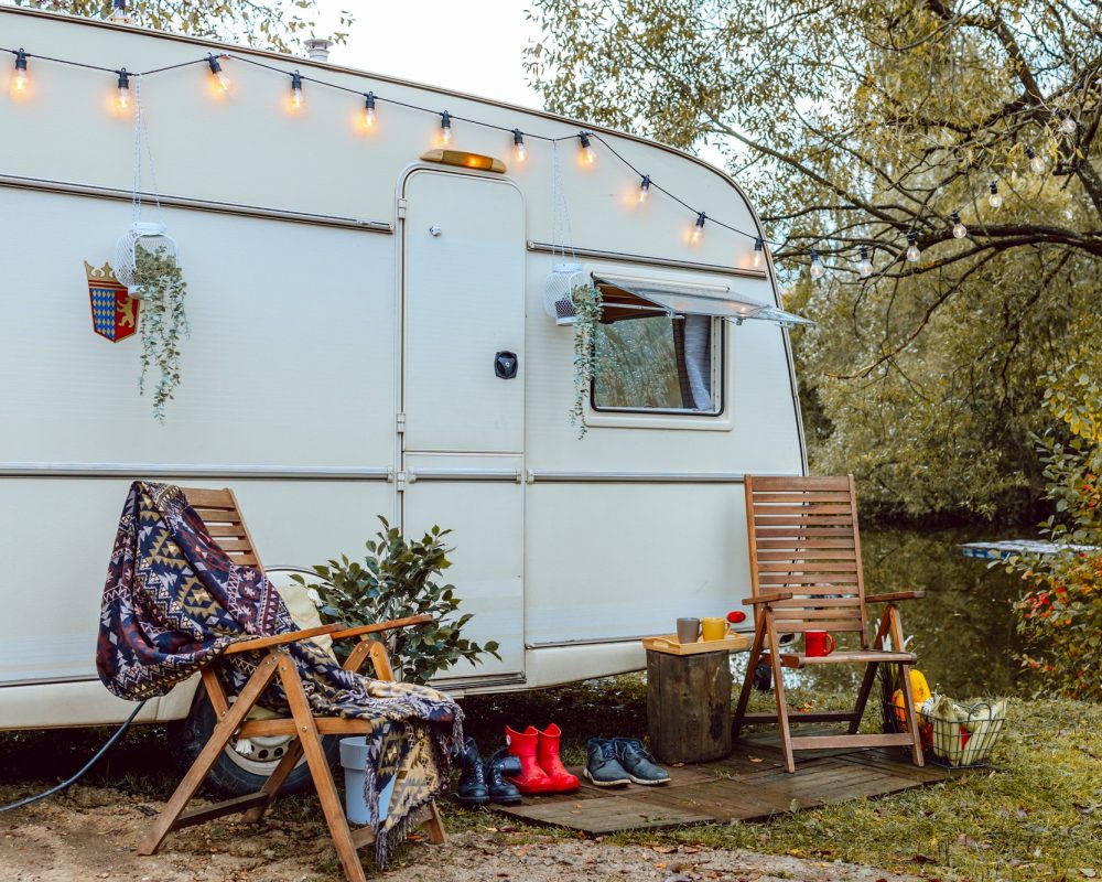 trailer-of-mobile-home-or-recreational-vehicle-stands-on-shore-of-pond-in-camping-in-autumn-concept